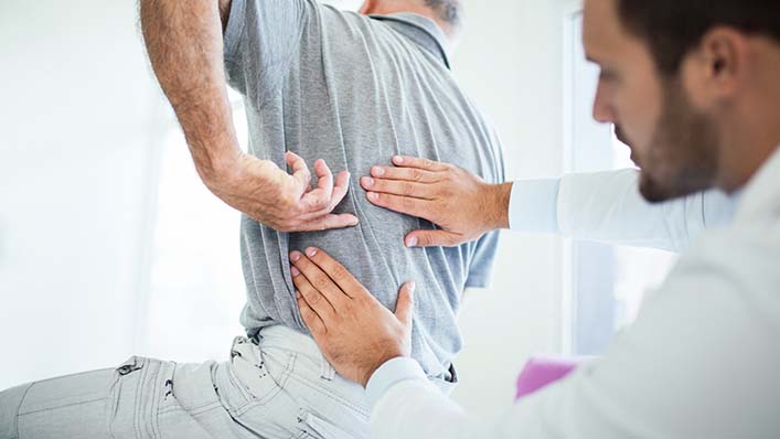 A doctor examines his patient's back during an appointment.